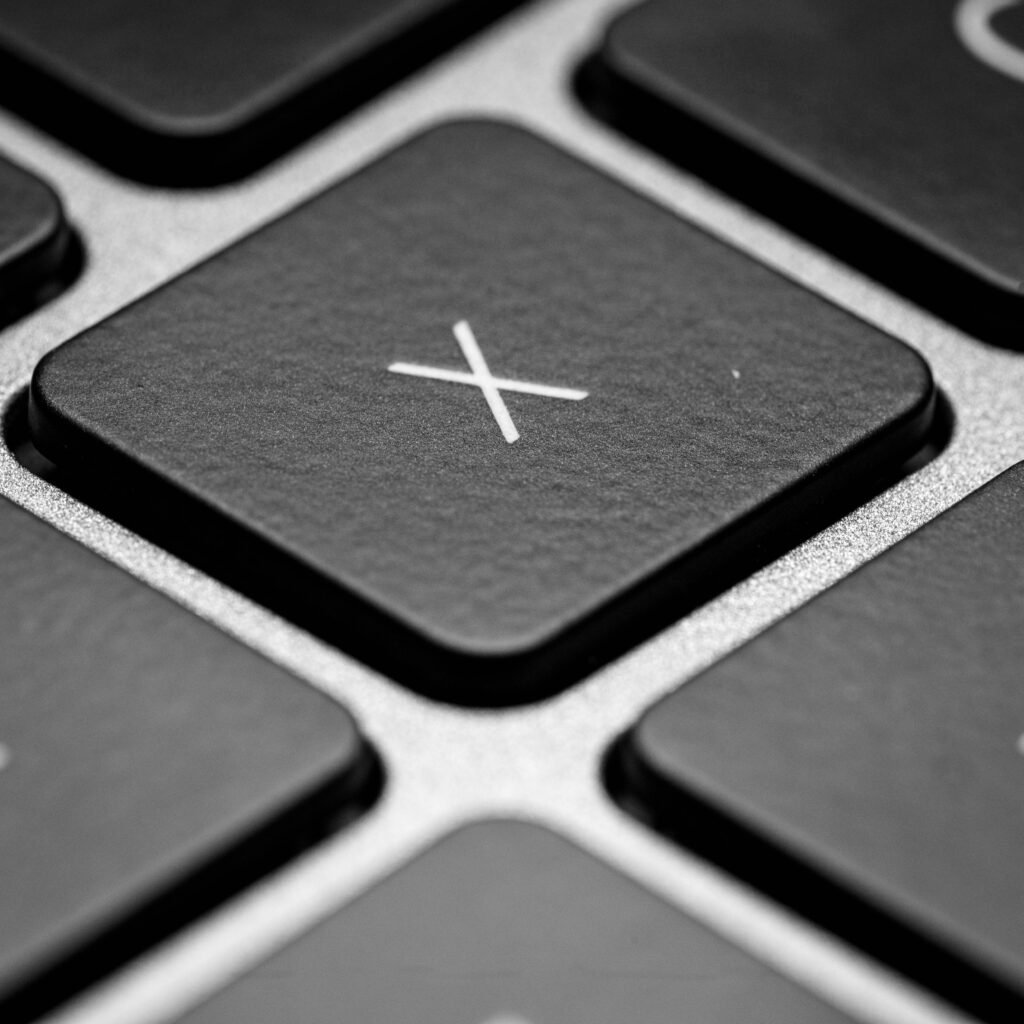 Detailed black and white close-up of a keyboard X key, showcasing texture and design.
